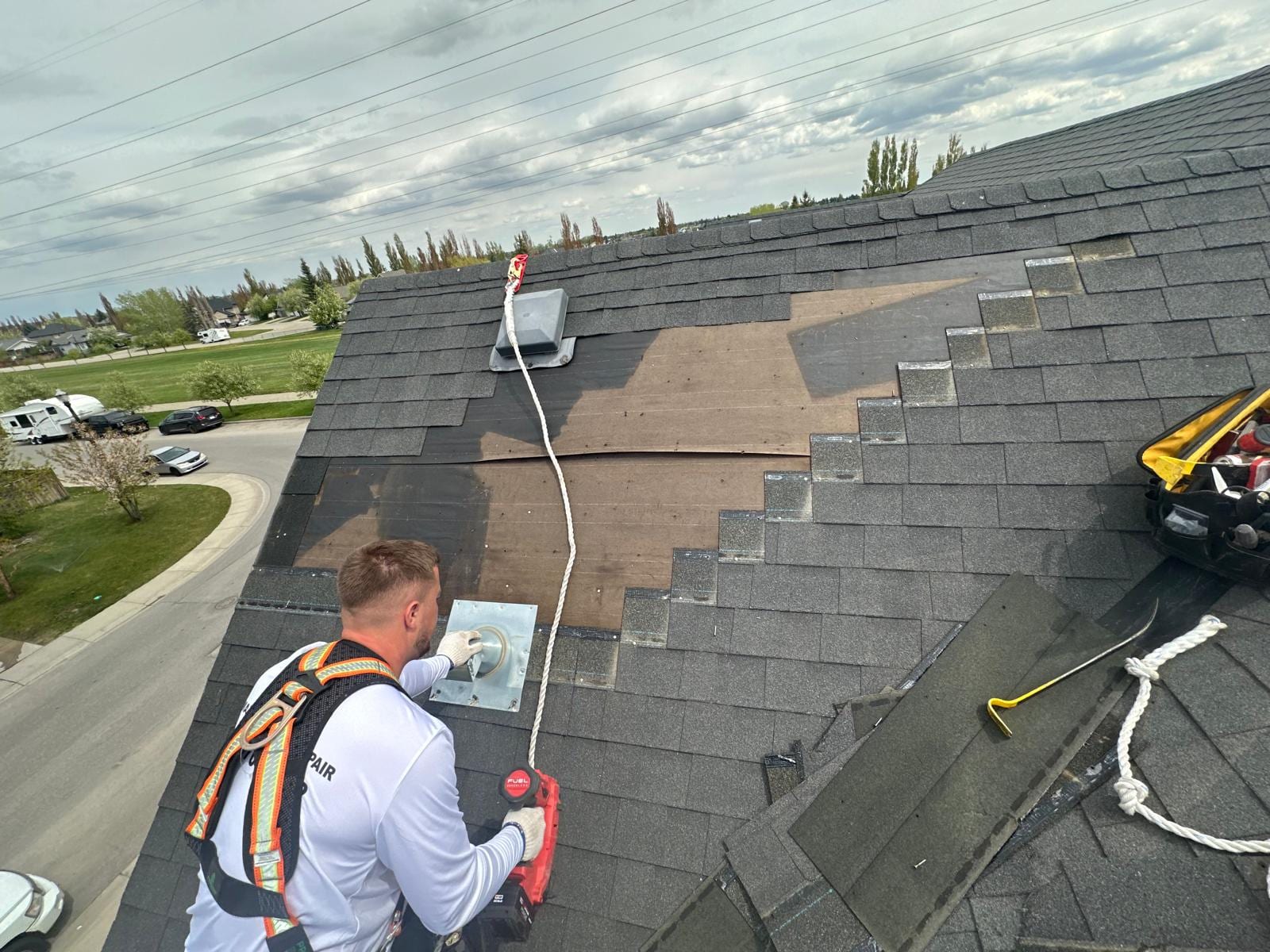 Kristjan Marku harnessed on a Calgary roof, replacing vent flashing during a shingle repair