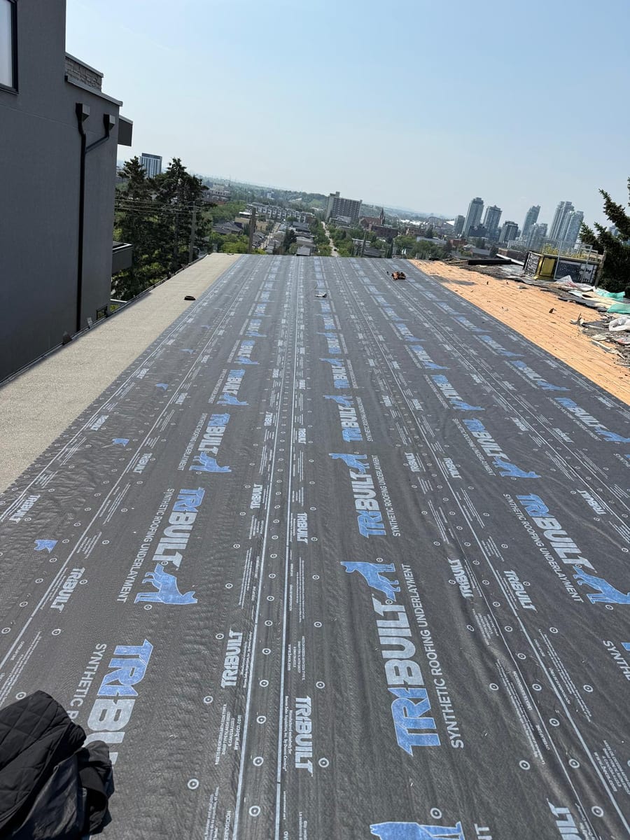 Branded synthetic underlayment rolled out over a roof deck in Calgary